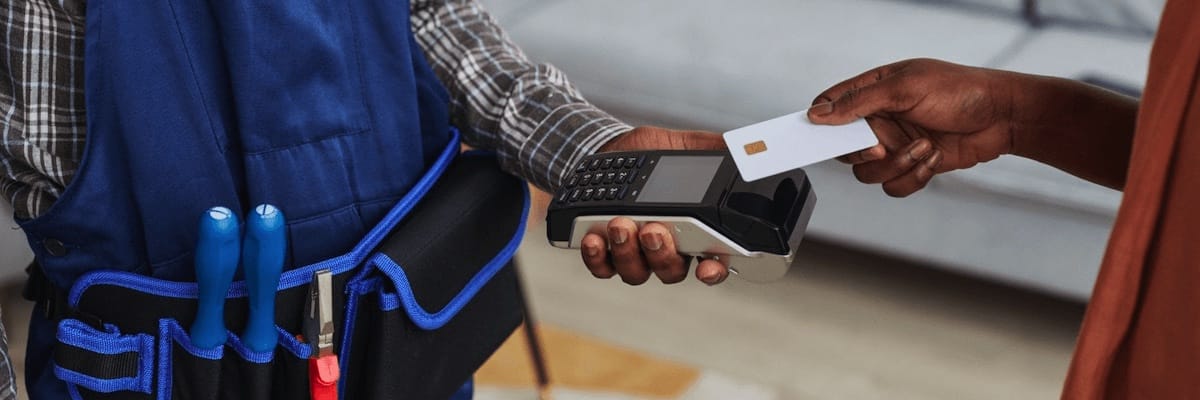 Service provider in a tool belt holding out a payment device as the customer taps their card on it